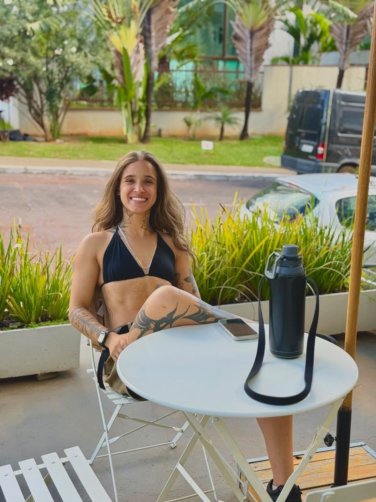 Layla Soares sentada em um café ao ar livre, sorrindo, em um dia comum